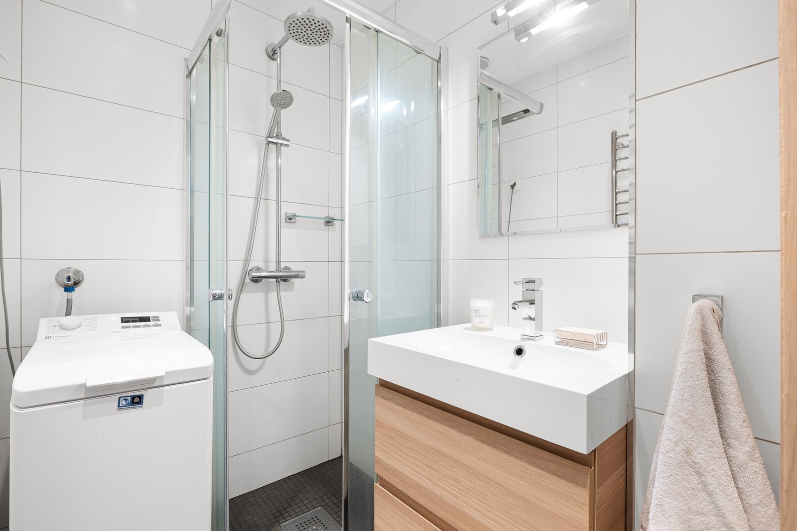Innredningen består av vegghengt toalett, servantskap med speil og belysning over, dusjnisje med skyvedører i glass og opplegg til vaskemaskin Galleribilde
