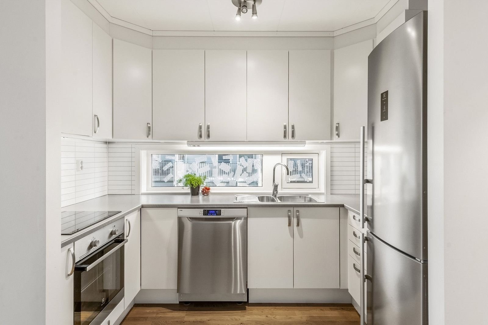 Pent kjøkken med innredning i hvite slette fronter og laminat benkeplate med nedfelt stål vask og ett greps blandebatteri Galleribilde