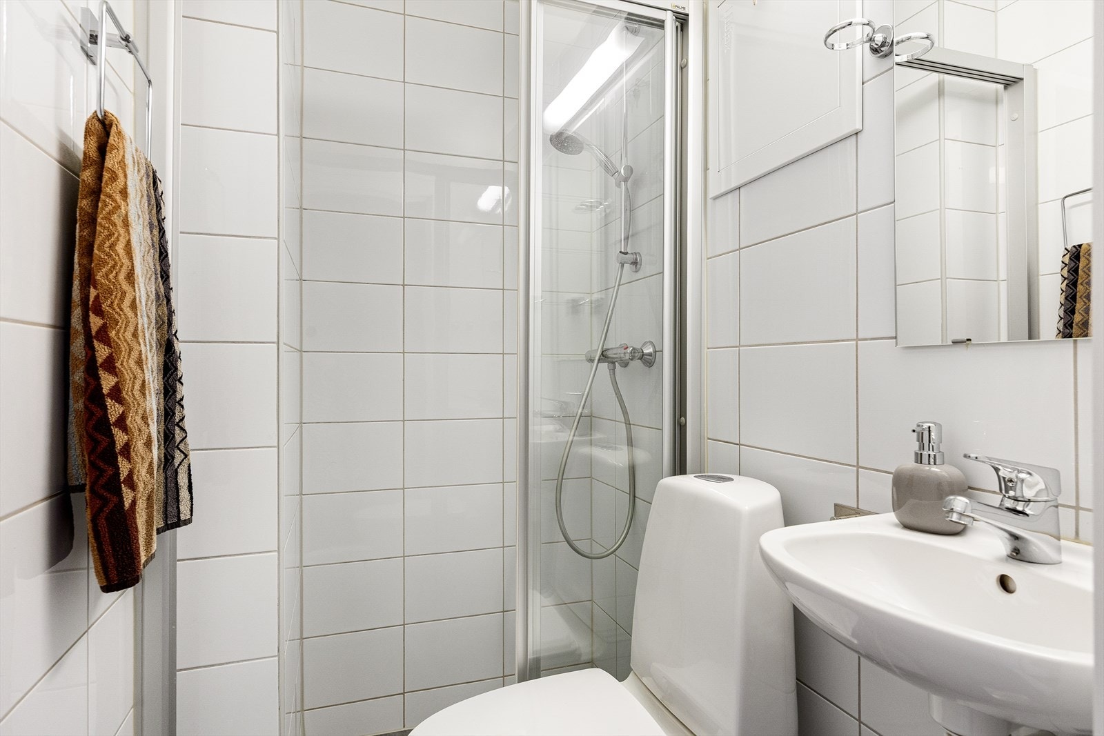 Badet er innredet med vegghengt servant med ettgreps armatur, speil på vegg med overlys og praktisk stikkontakt samt toalett. Galleribilde