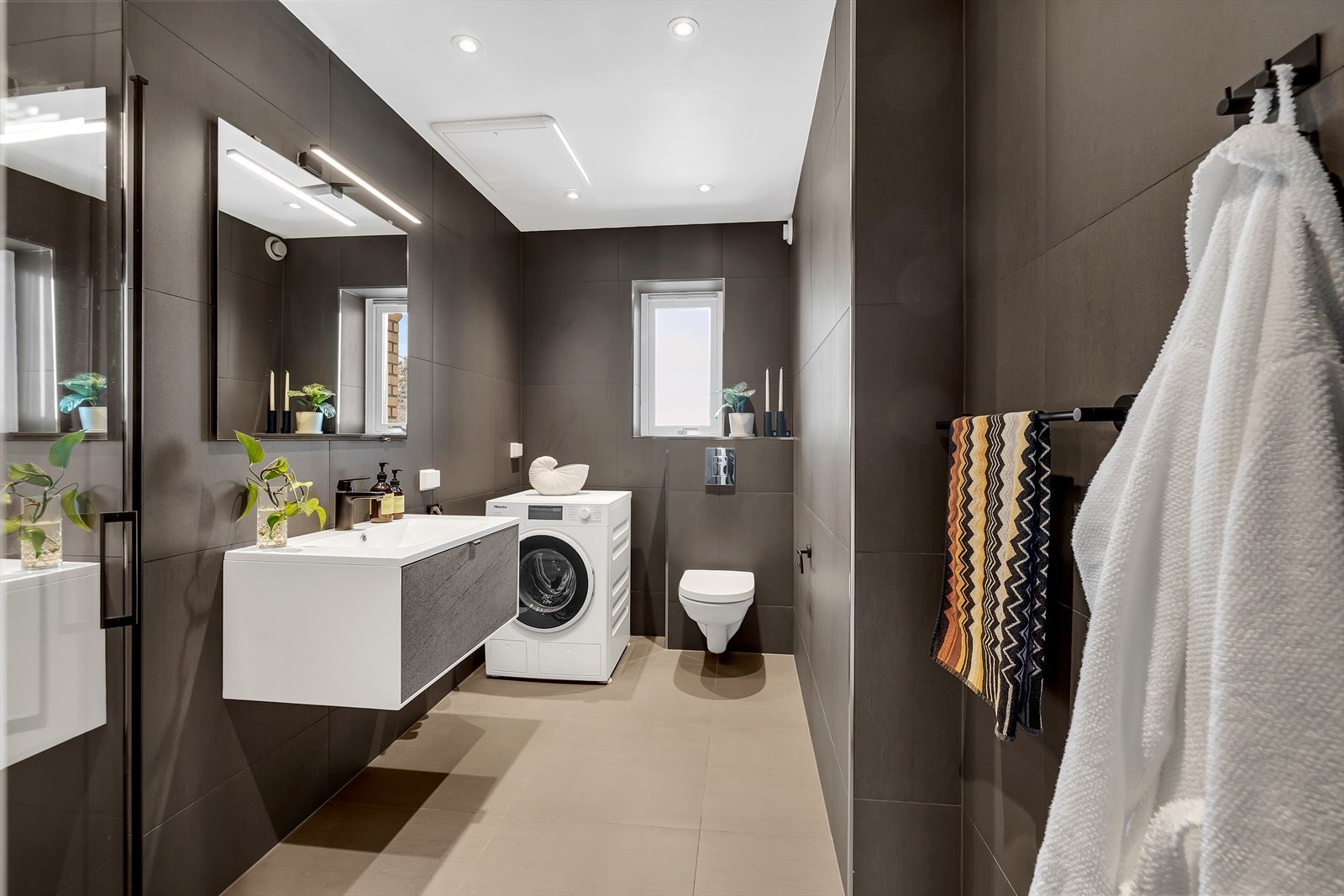 Badet har flislagte vegger og gulv med gulvvarme. Baderomsinnredning med servant på underskap og speil med belysning over. Galleribilde