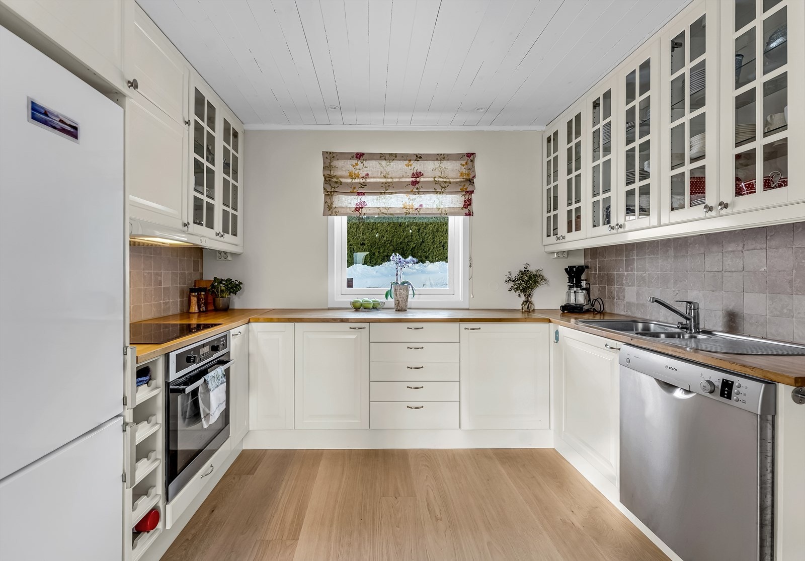 Kjøkkeninnredning fra 2008, med hvite, profilerte skapfronter - noen med glassfelt og integrert belysning. Galleribilde