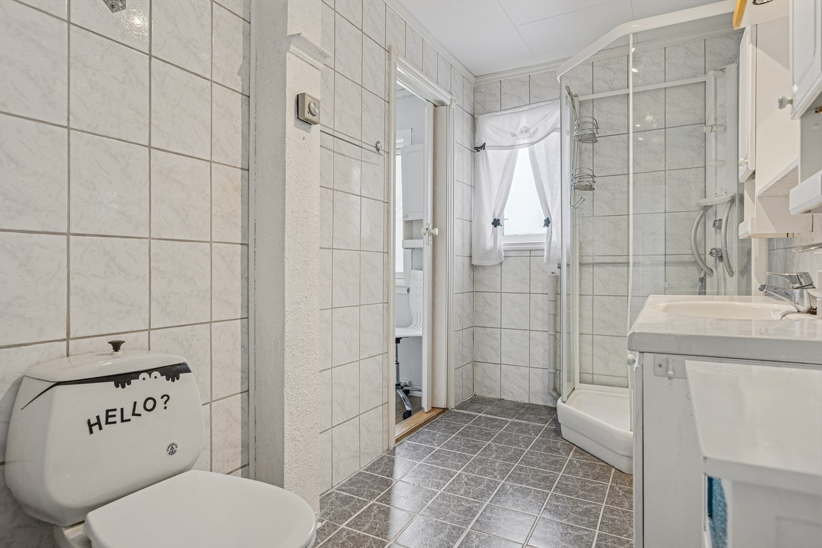 Badet er utstyrt med dusjkabinett, gulvstående toalett, opplegg for vaskemaskin og en lys baderomsinnredning. Galleribilde