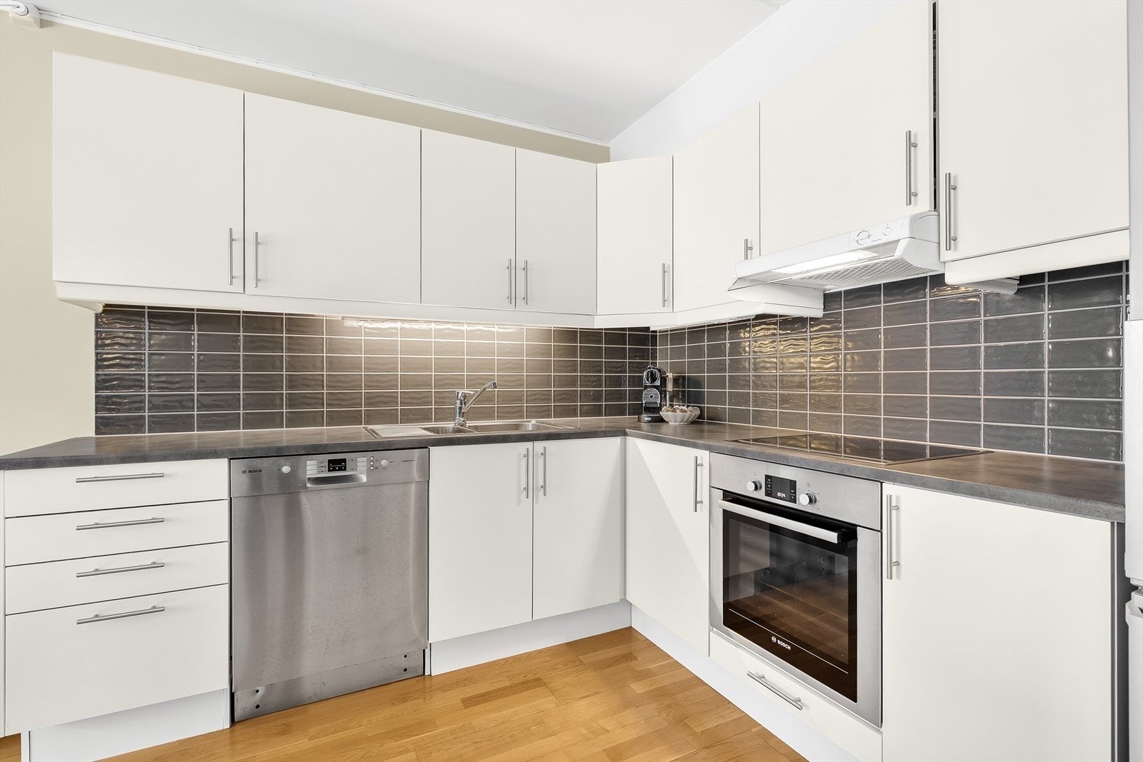 Kjøkkenet har vinklet innredning med slette fronter, laminat benkeplate og flislagt vegg. Galleribilde