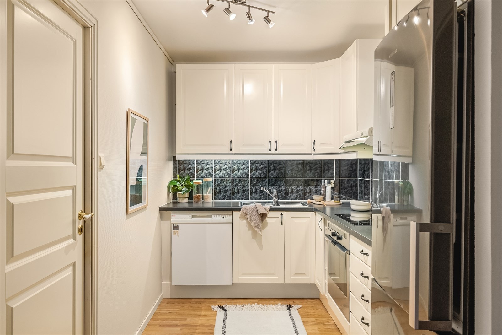 Kjøkkenet ligger i delvis åpen løsning med stue. Innredning med tidløse, profilerte skapfronter og fliser over laminert benkeplate. Galleribilde