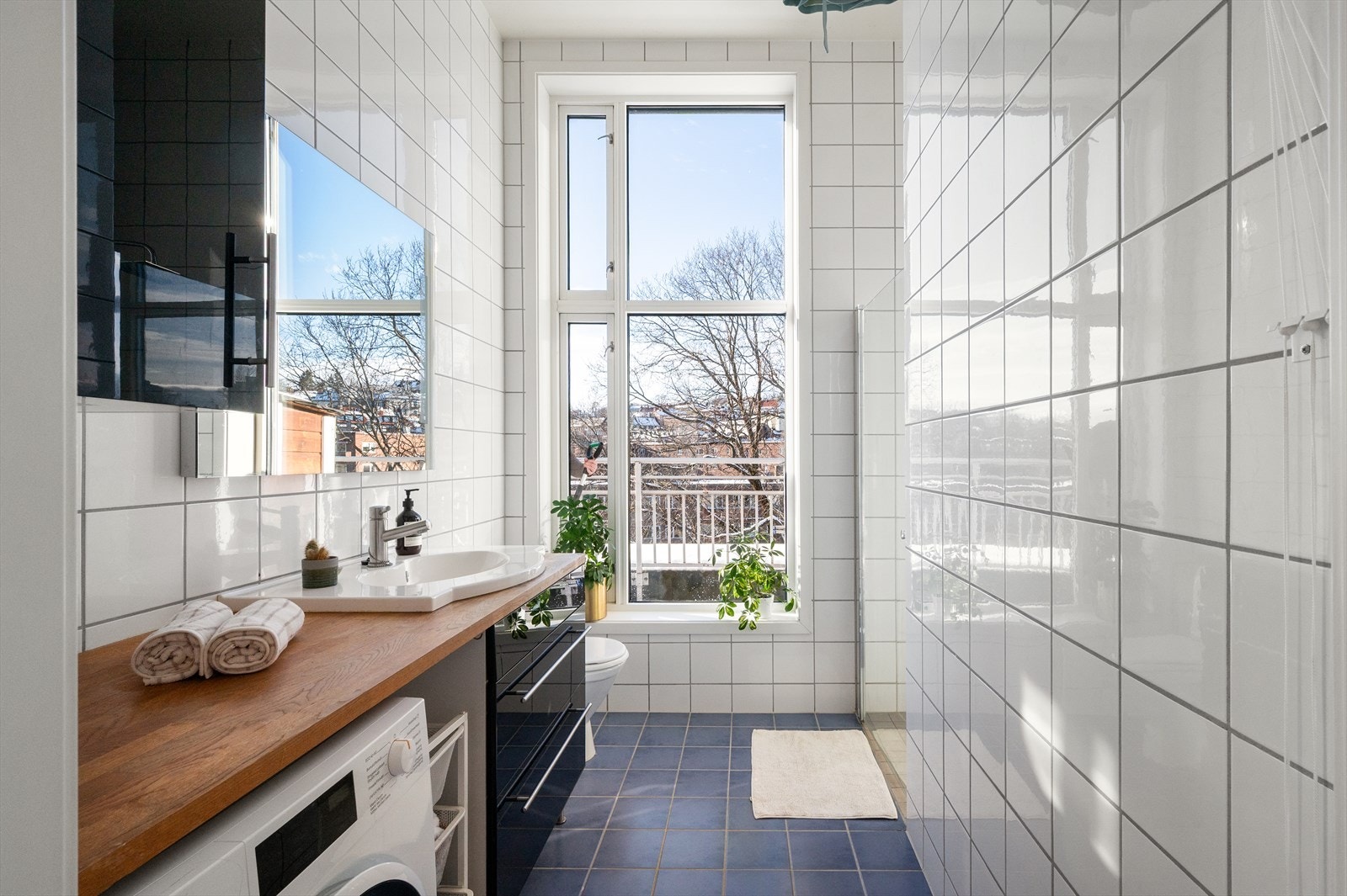 Flislagt bad med mye lys og opplegg for vaskemaskin under benkeplate. Galleribilde