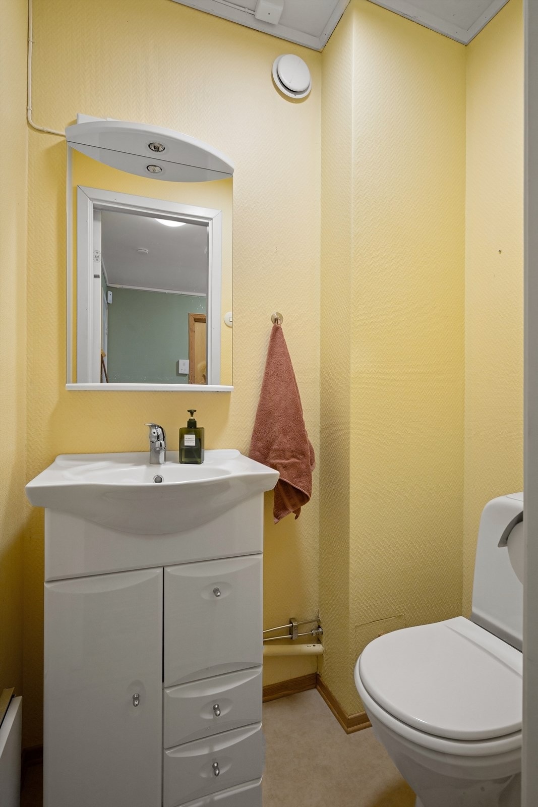 Toalettrommet er innredet med gulvstående toalett og servant med skuffeinnredning og speil over Galleribilde