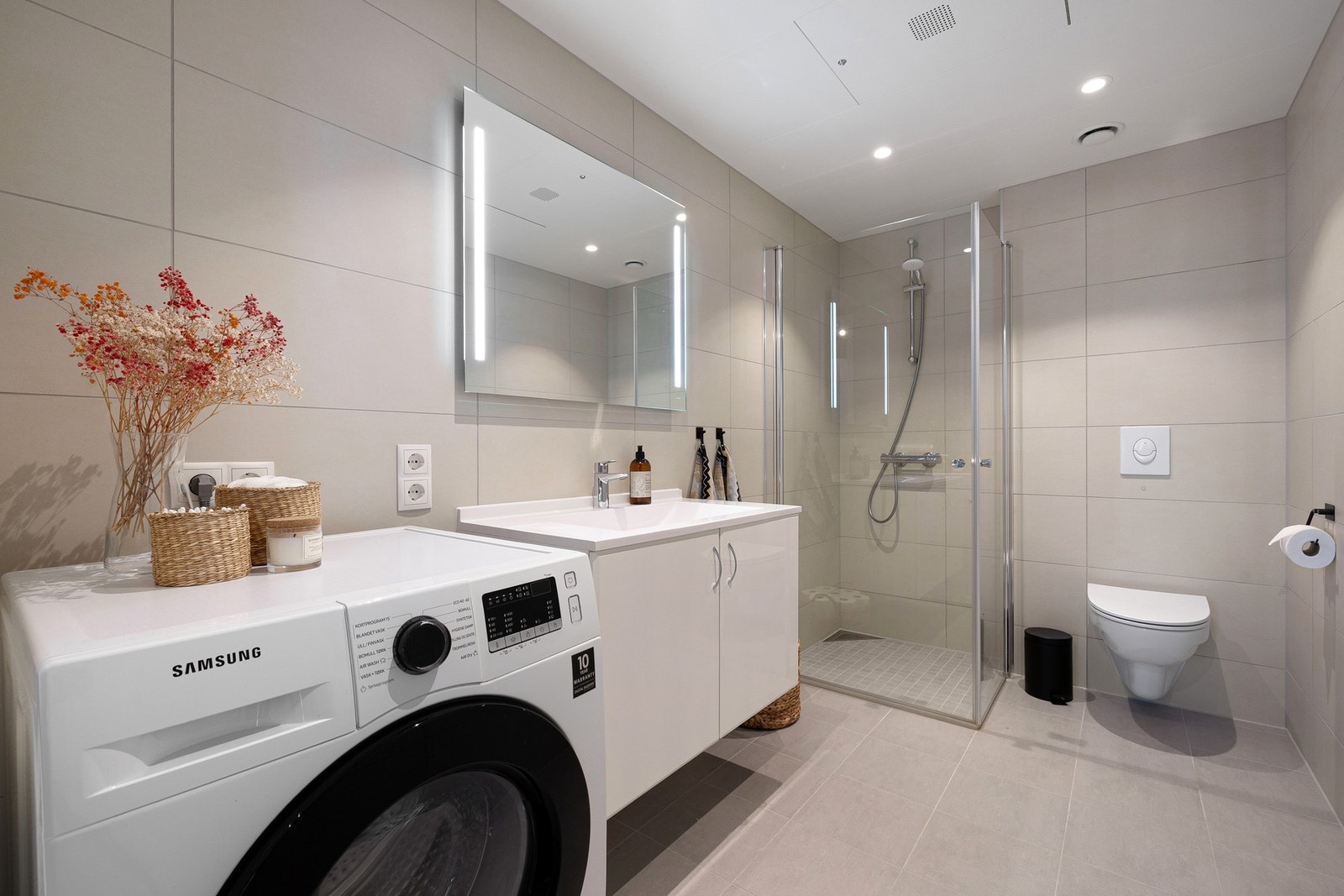 Badet har egenskaper som elektriske varmekabler i gulv, innfellbare og plassbesparende dusjdører i glass, kran og avløp for vaskemaskin, servant med underskap, samt speil med innfelte lys. Galleribilde