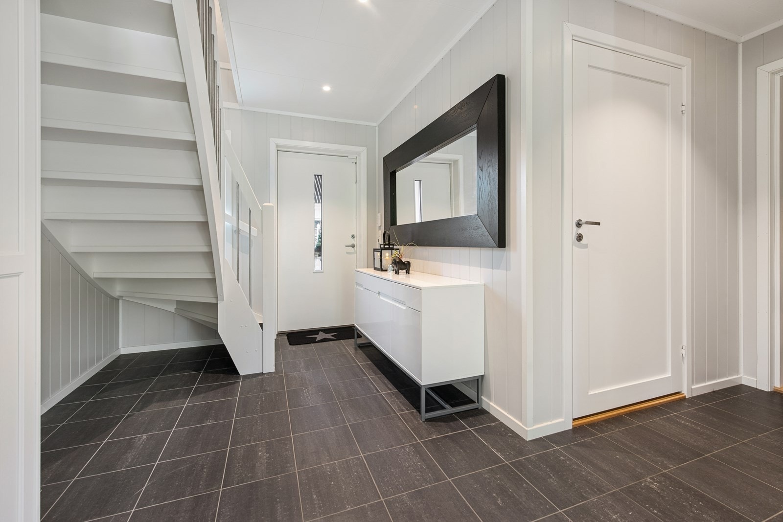 Romslig og delikat entré med flislagt gulv, lyse vegger og spotter i tak. Et funksjonelt og representativt rom med god plass til oppbevaring og en lun velkomstfølelse. Galleribilde