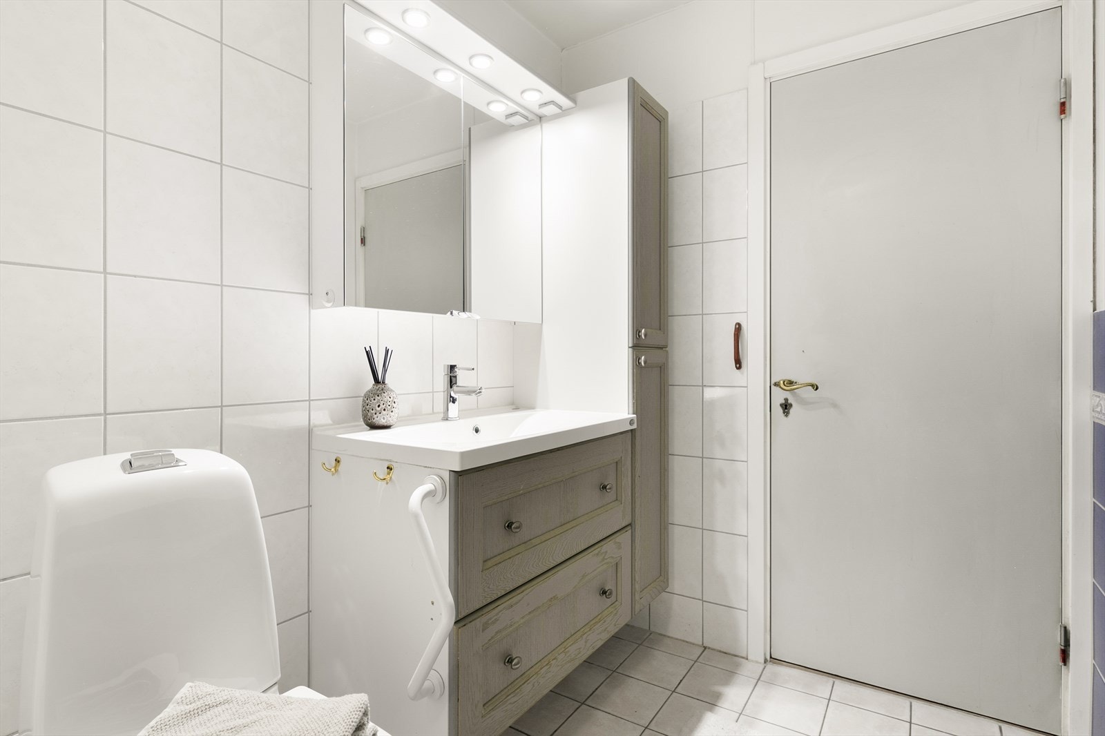 Flislagte overflater innredet med en servant, speil m/lys og plass til oppbevaring. Galleribilde