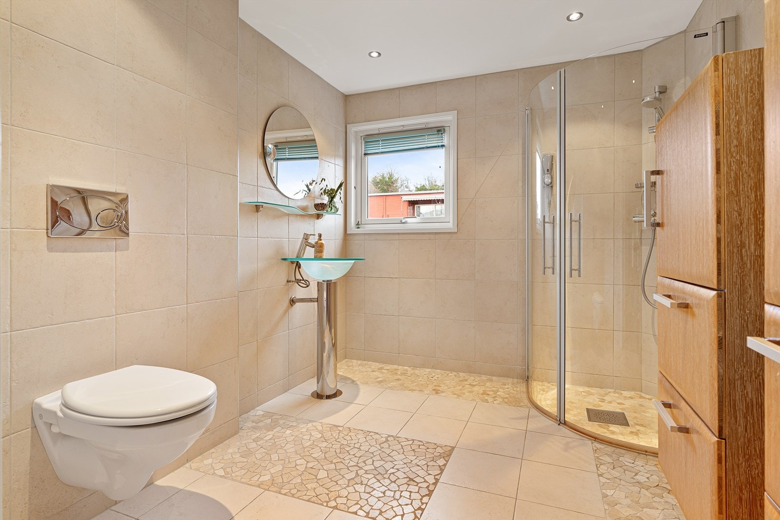 Lekkert bad på 6m² med søylevask i glass og åpen dusjløsning med innfellbare dører. Oppvarmes med varmekabler i gulv og ventileres med mekanisk avtrekk. Galleribilde