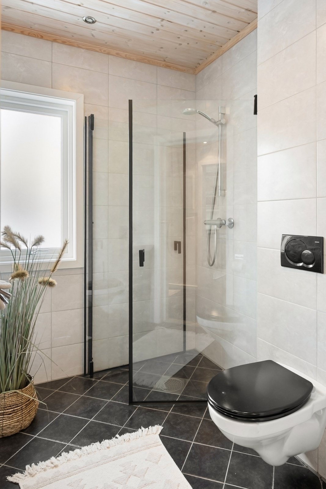 Dusjhjørne med nyere dusjdører, vegghengt toalett og servant med underskap. Galleribilde