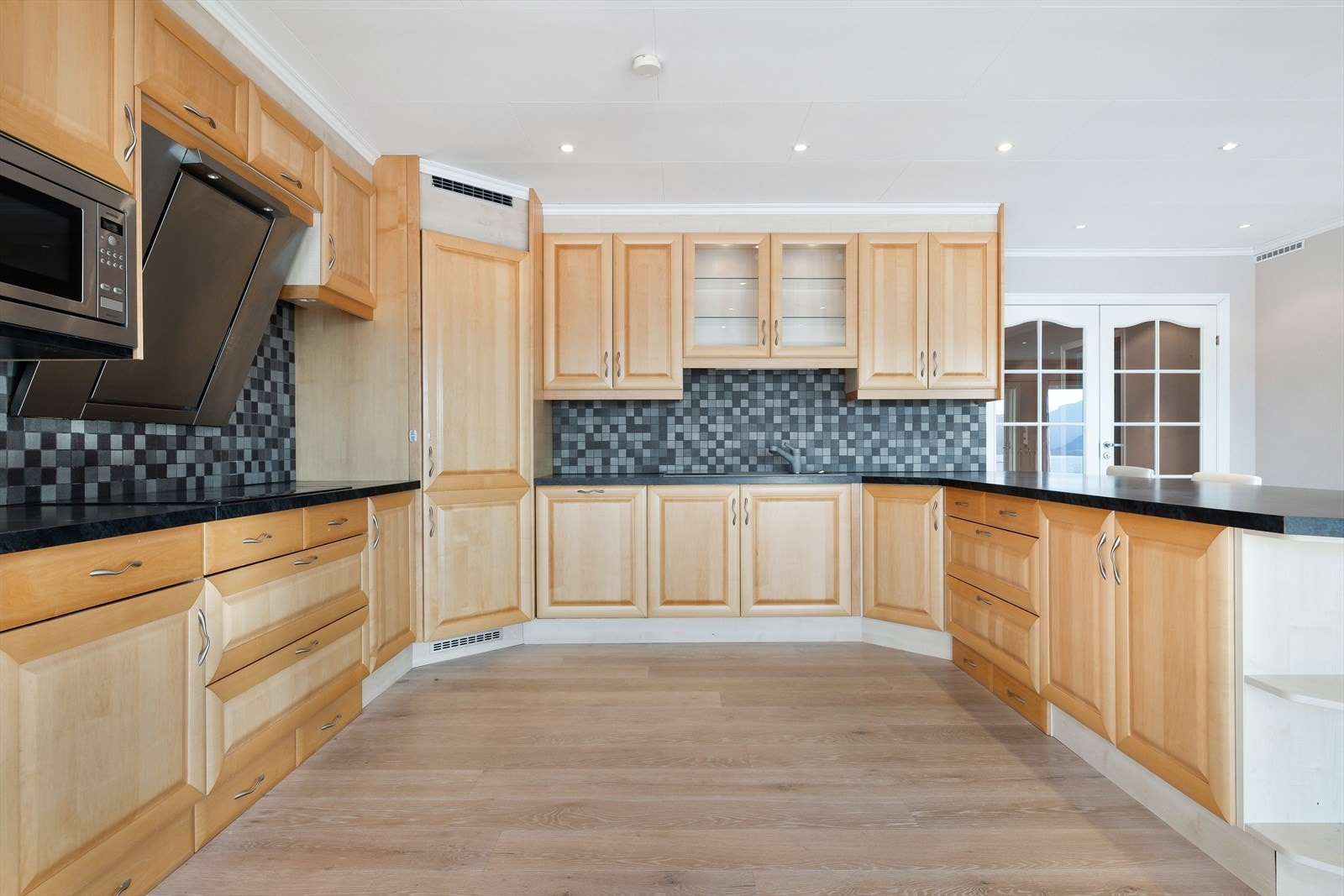 Kjøkkenet fremstår som boligens naturlige samlingspunkt - romslig, funksjonelt og stilrent utført i en varm trefarget innredning. Galleribilde