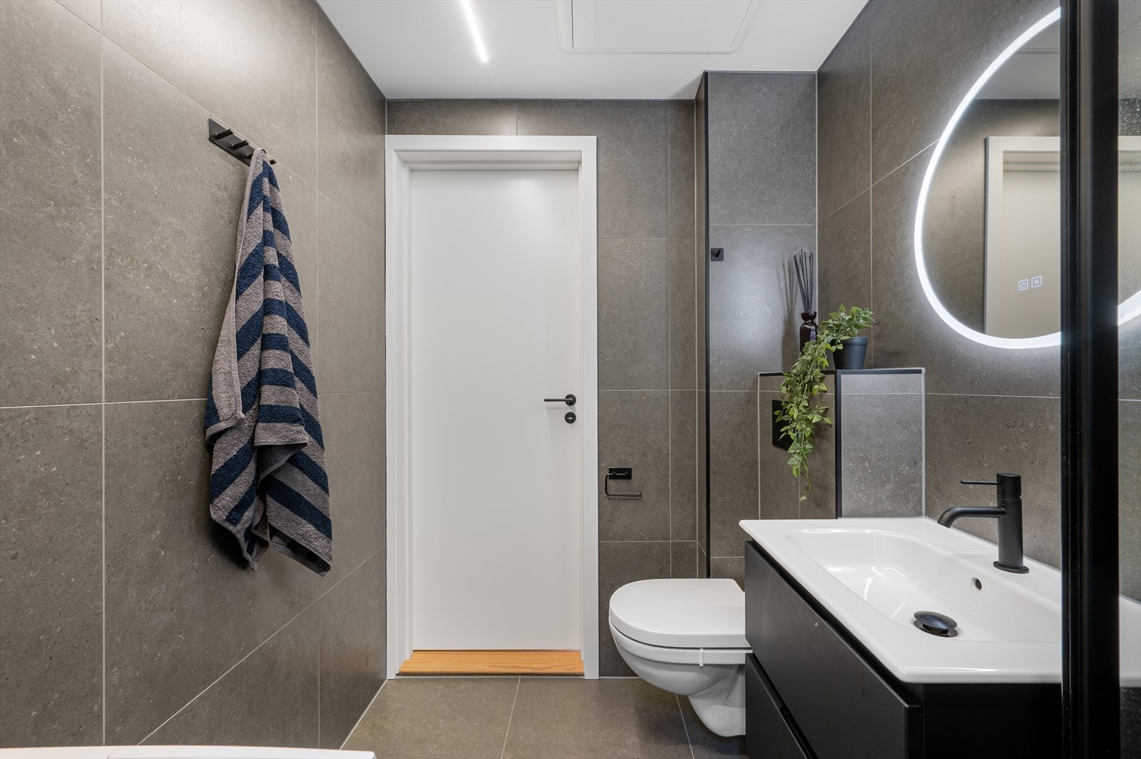 Badet er innredet med vegghengt toalett, dusjhjørne m/glassdører, opplegg for vaskemaskin og servant med innredning/speil/belysning Galleribilde