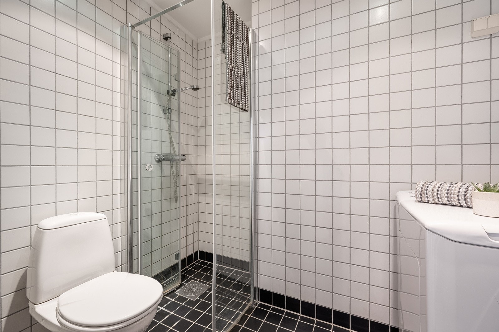 Baderommet er utstyrt med vegghengt servant med speil og belysning over, dusjhjørne med glassdører og gulvstående toalett. I hjørnet er det plass og opplegg for vaskemaskin. Galleribilde