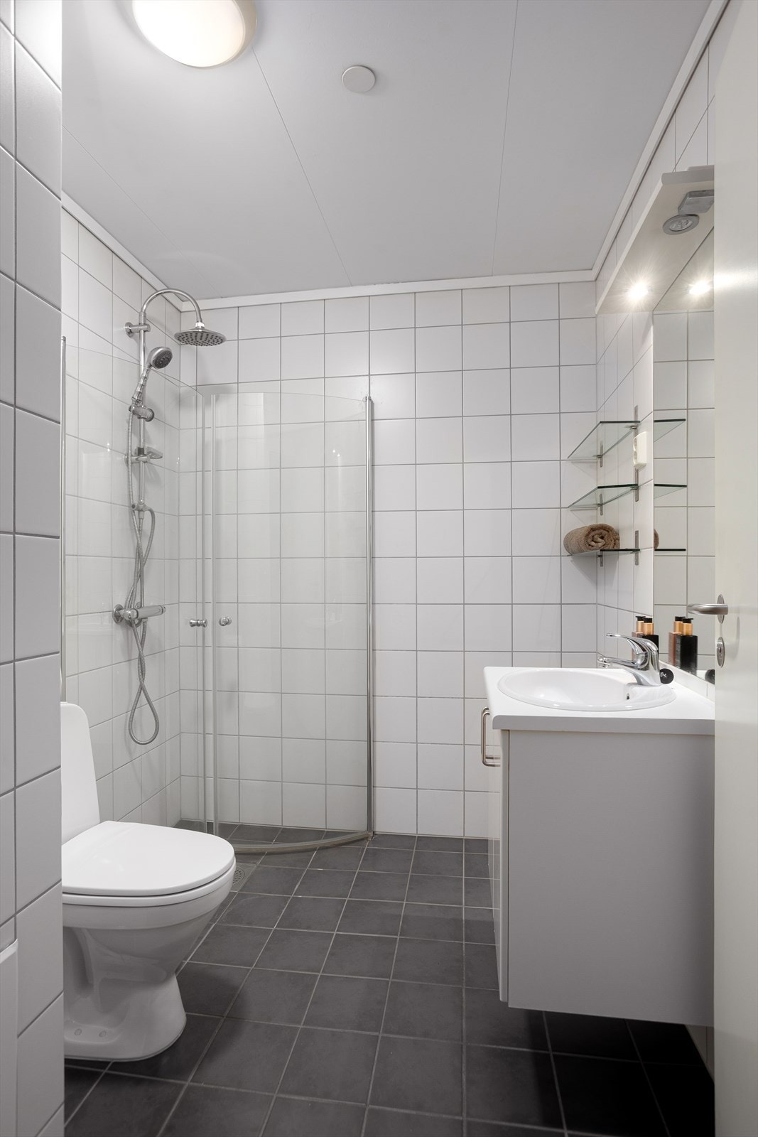 Badet har servant med skuffeseksjon, speil med lys, buet dusjhjørne og toalett Galleribilde