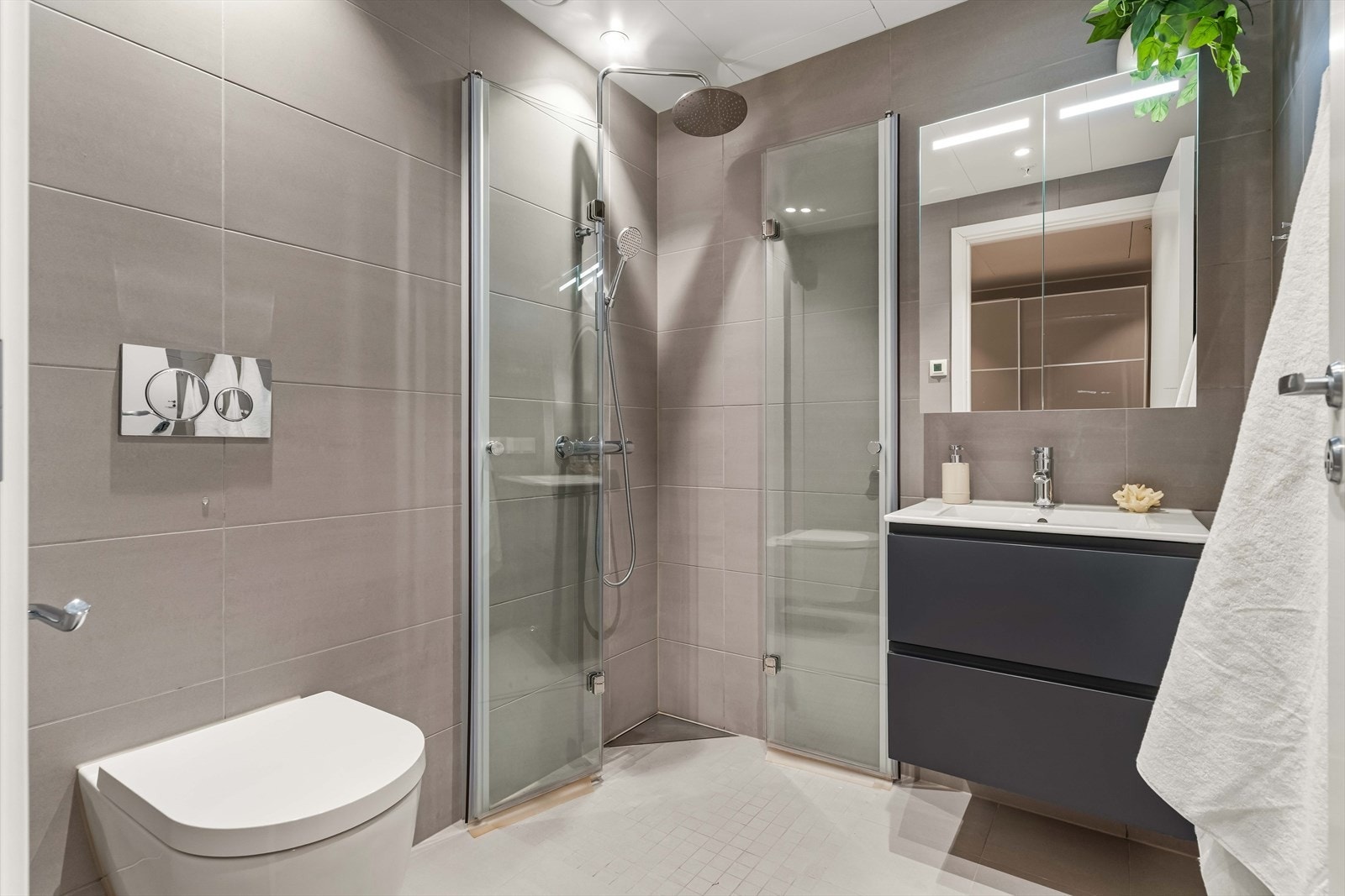 Flislagt bad med moderne innredning, dusjhjørne med innfellbare glassdører og vegghengt toalett. Tidløse materialvalg og god belysning. Galleribilde