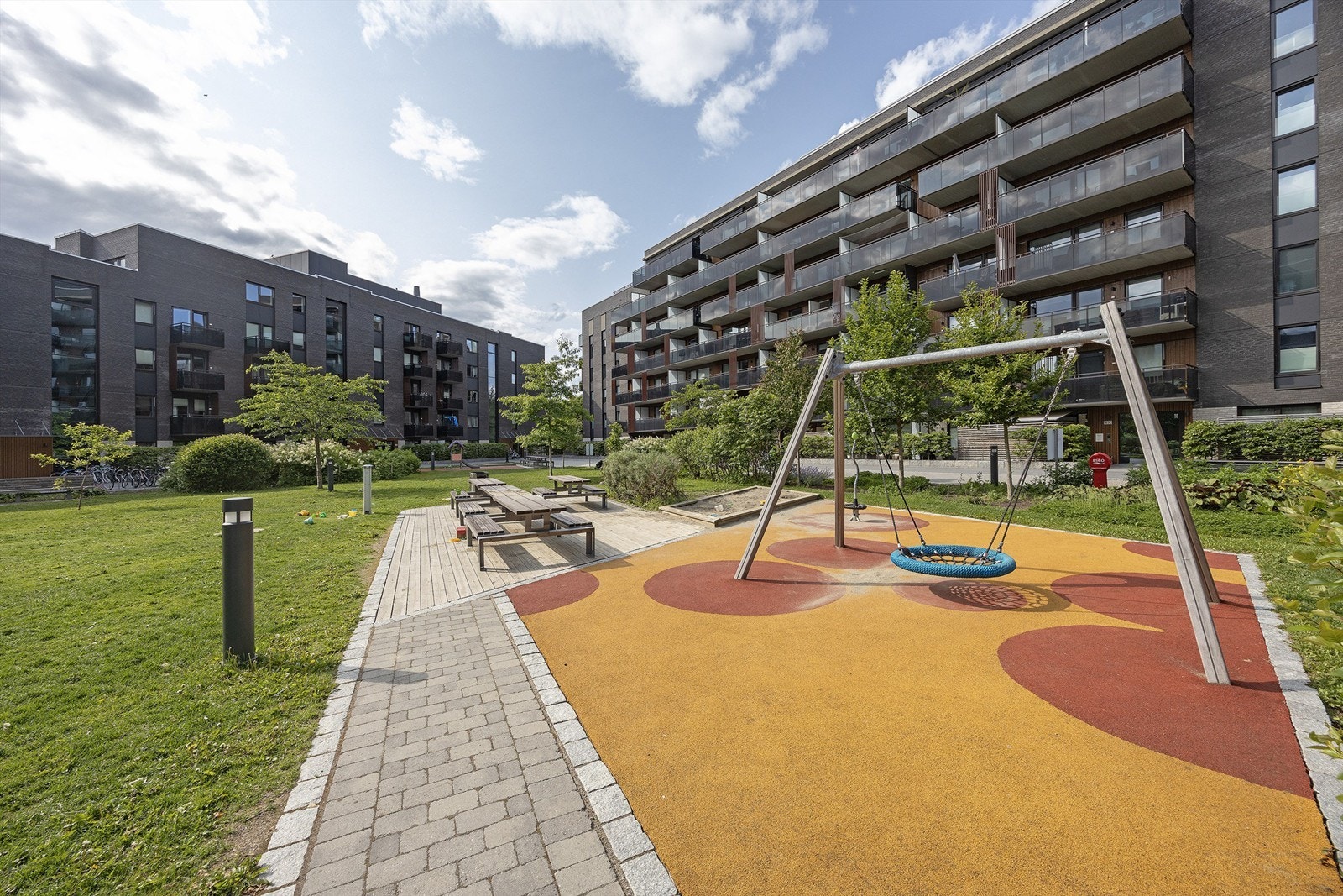 Nydelig felles indre gårdsrom med lekeapparater, sittebenker og grill, sykkelparkering, asfalterte lysbelagte stier og grønne områder med gressplen, prydbusker, trær og diverse beplantning Galleribilde