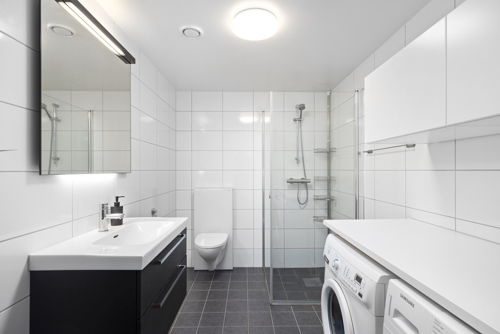 Innbydende og meget romslig bad med hvite fliser på vegg og grå fliser med varme i gulv Galleribilde