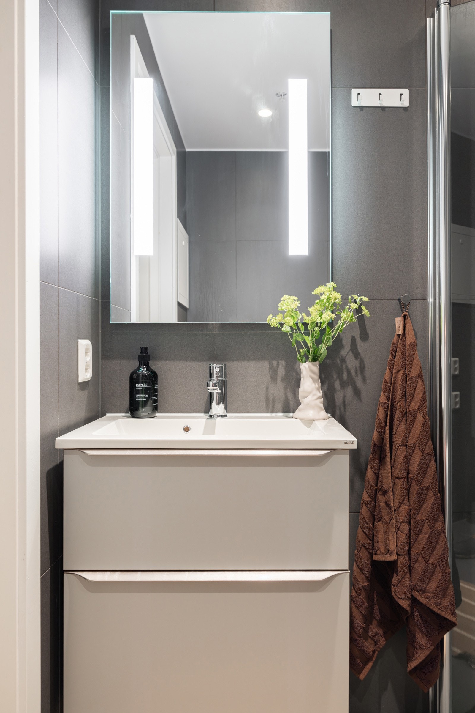 Moderne baderomsinnredning med skuffer og heldekkende servant, speil med integrert belysning over. Galleribilde