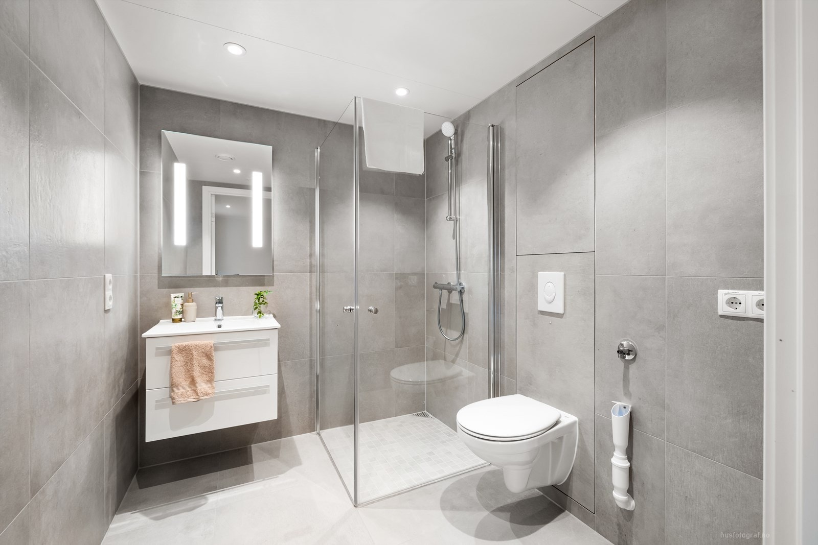 Badet - Her har man en heldekkende servant med underskap, speil på vegg, dusjnisje med innfellbare dører og veggmontert toalett Galleribilde