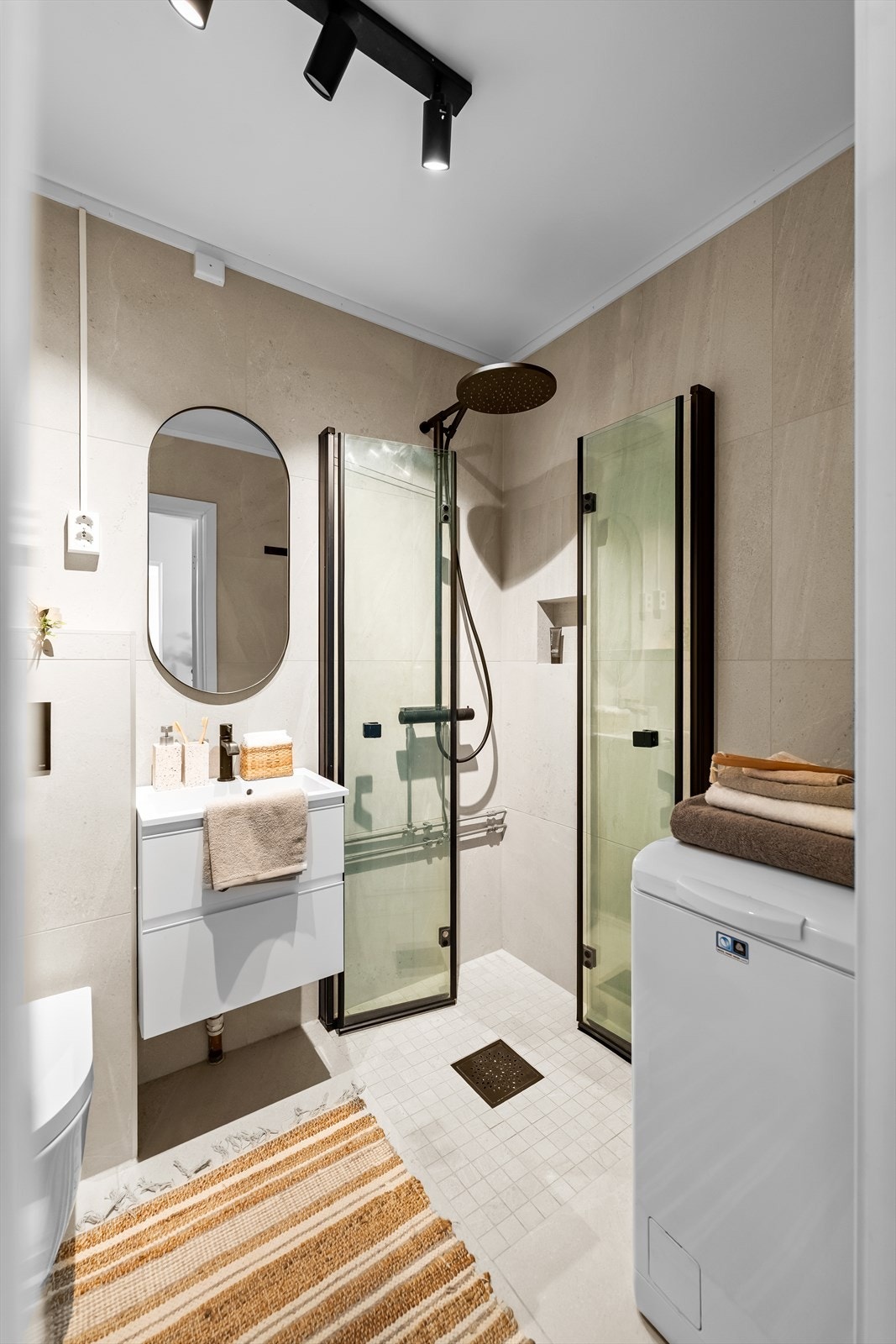 Moderne innredning med nedfelt servant, veggmontert toalett, dusjhjørne med glassvegger og opplegg for vaskemaskin. Galleribilde