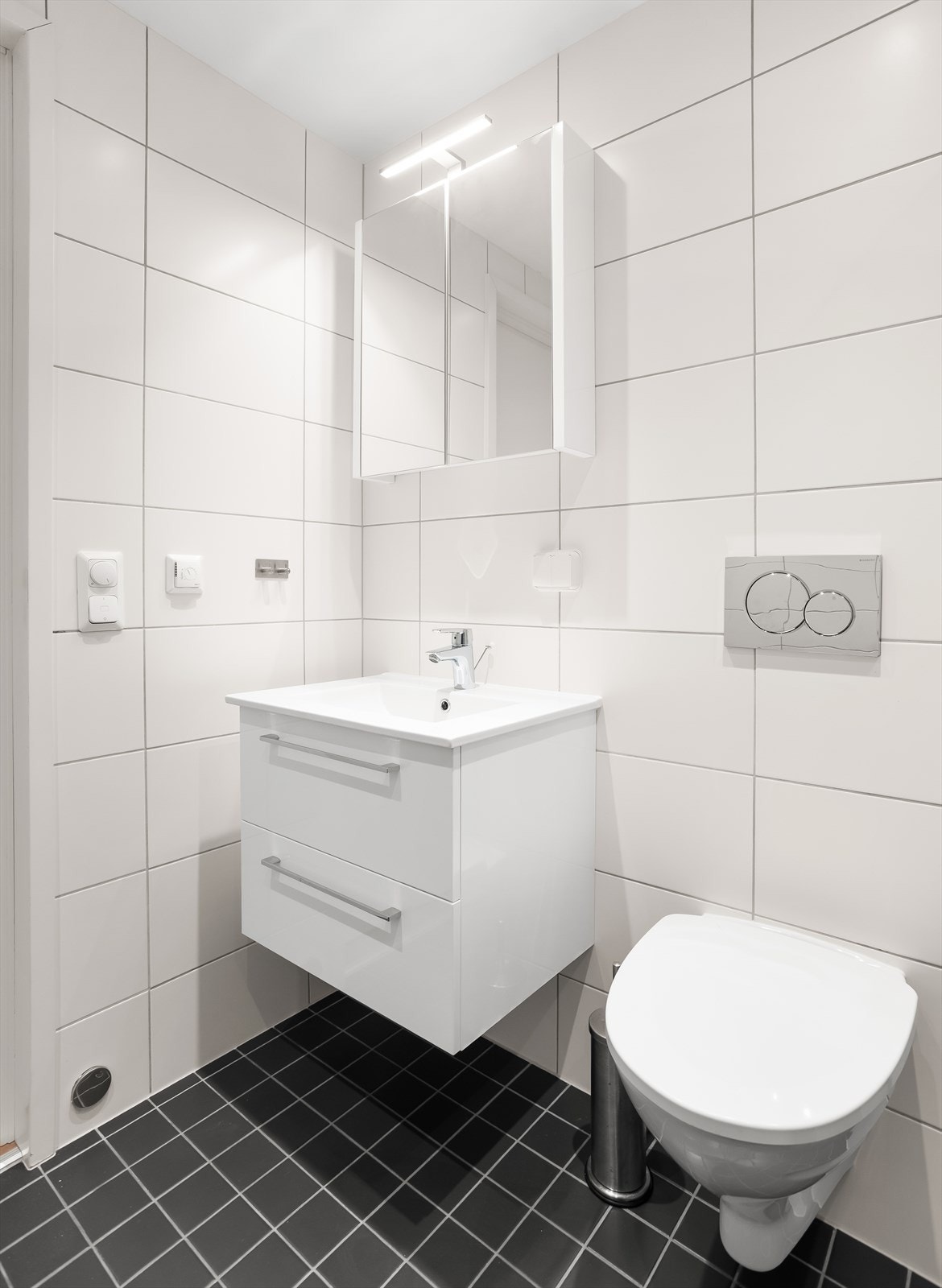 Badet er utstyrt med vegghengt toalett, servantskap og dusjhjørne med innfellbare dører. Galleribilde