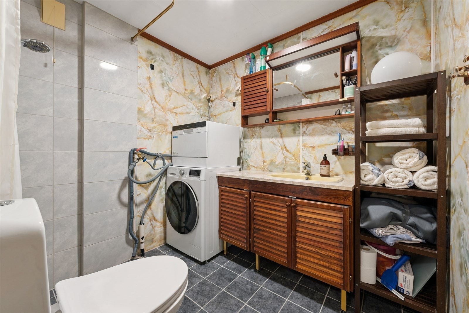 Badet i kjelleretasjen er av eldre alder og har flislagt gulv, samt fliser og våtromsplater på vegg. Utstyrt med nedfelt servant på underskap, klosett og dusj. Galleribilde