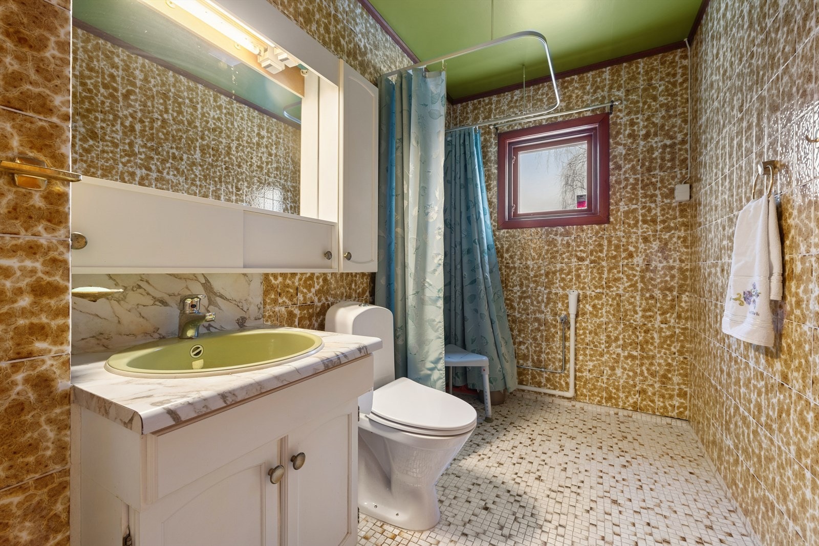 Boligens bad er av eldre alder med fliser på gulv og vegger. Utstyrt med heldekkende servant med underskap, speil, klosett og dusj. Galleribilde