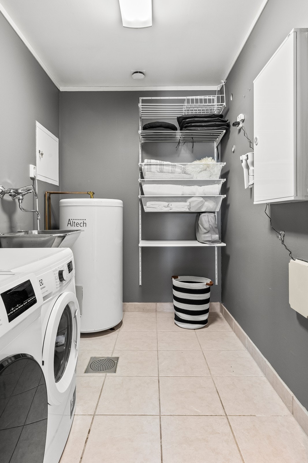 Praktisk vaskerom med flislagt gulv med gulvvarme og utslagsvask Galleribilde