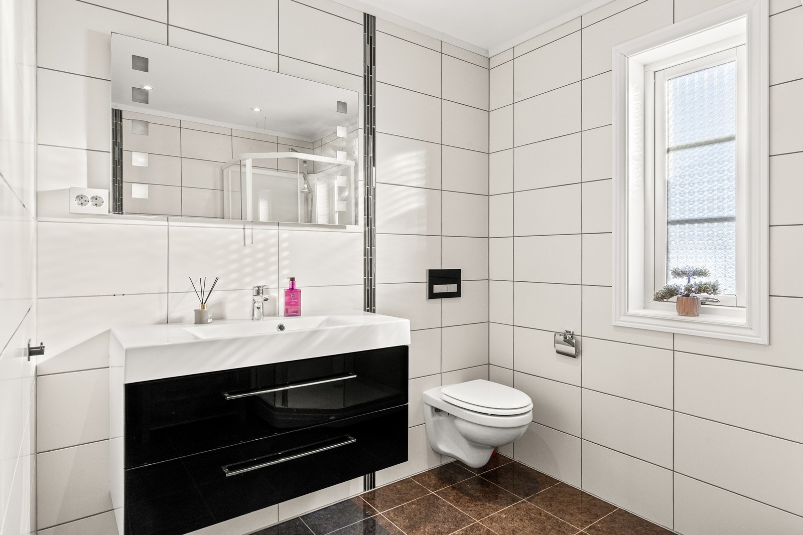 Badet har flislagte overflater, vegghengt toalett og servantinnredning med skuffer. Galleribilde