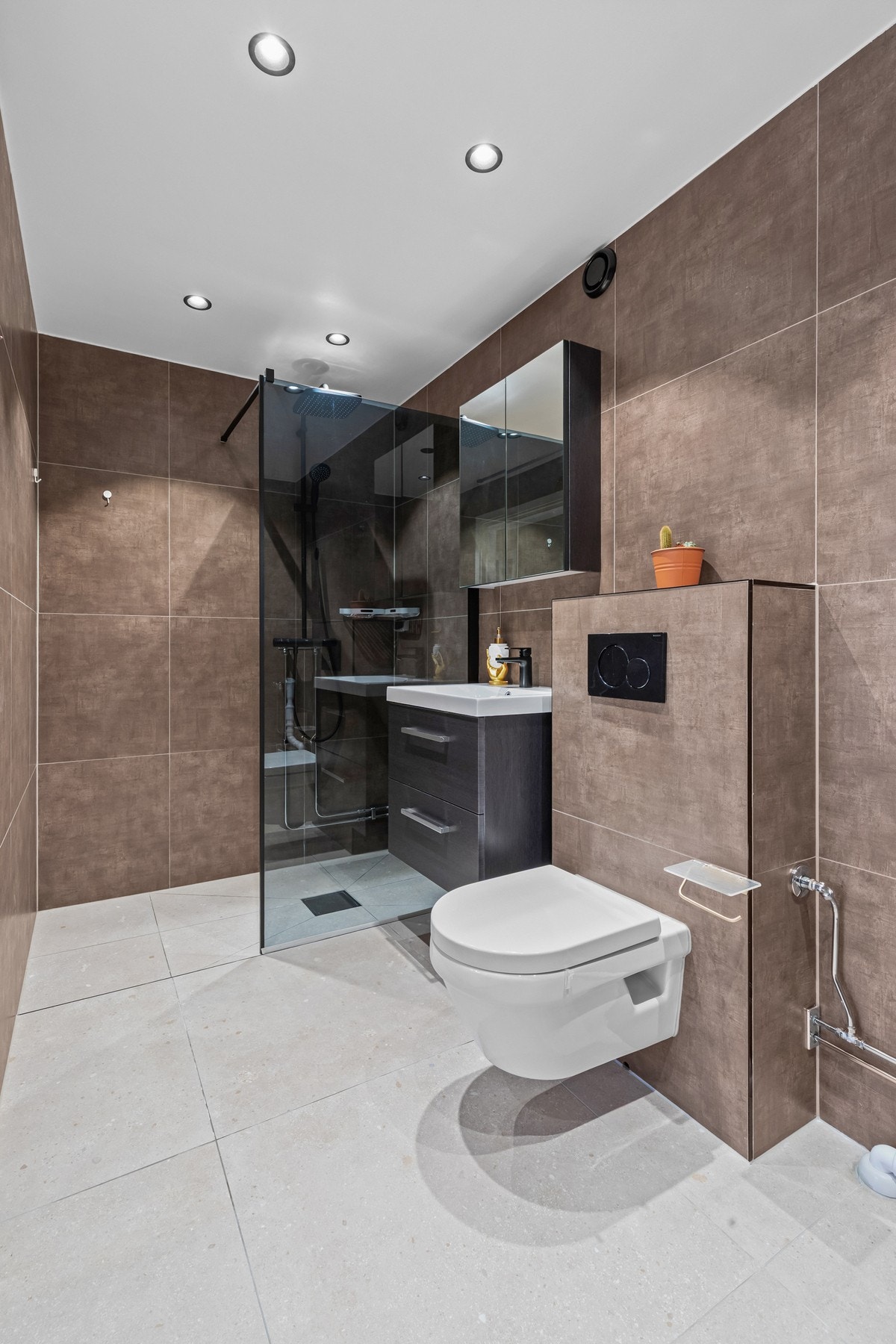 Romslig baderom med opplegg for vaskemaskin, mekanisk avtrekk og gjennomgående fliser som skaper en helhetlig og tidløs stil. Galleribilde