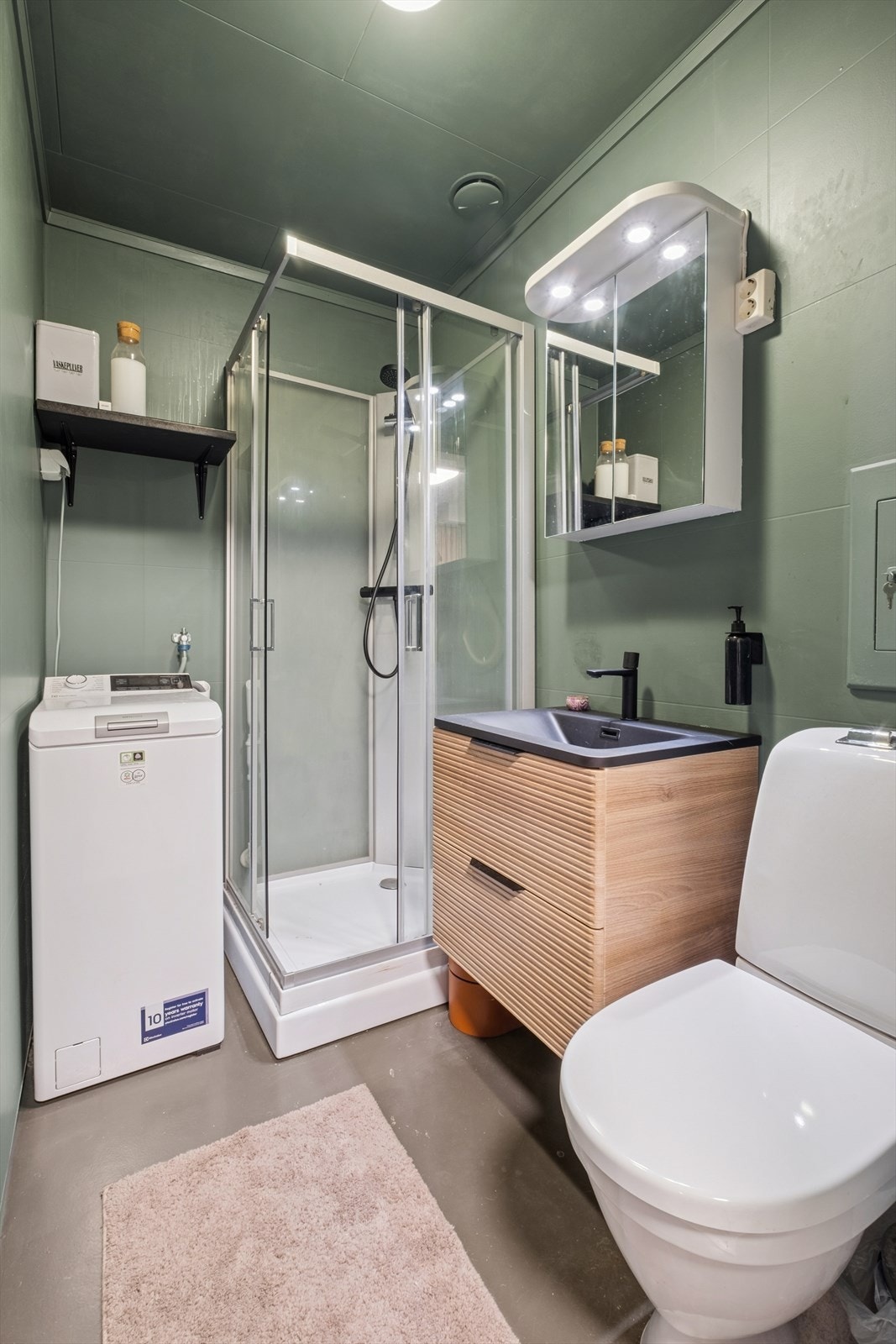 Baderommet er utstyrt med wc på sokkel, servantinnredning, dusjkabinett og opplegg for vaskemaskin. Det er malte plater i himling samt tapetserte vegger, og gulvet er belagt med belegg. Badet er fra byggeår. Galleribilde