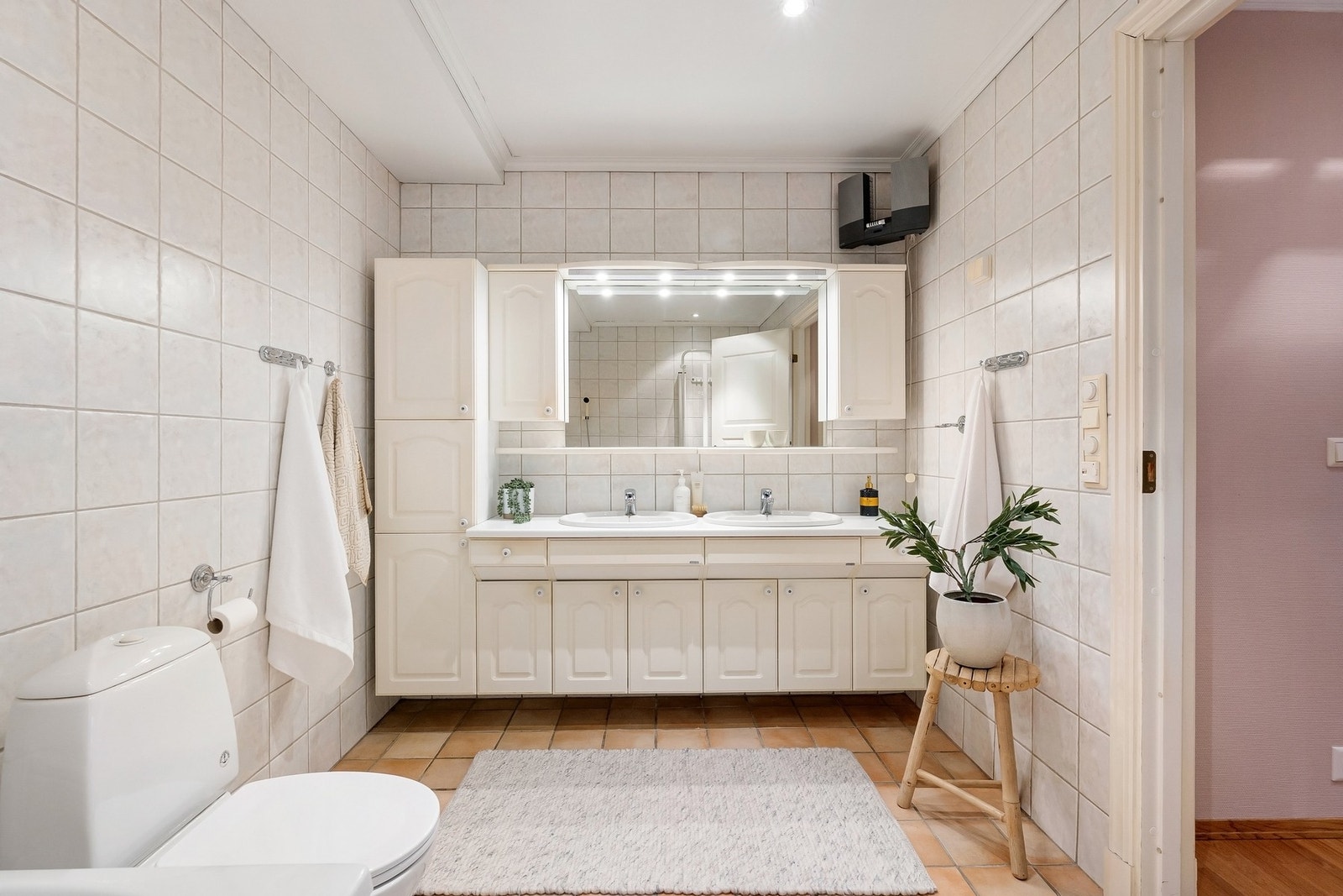 Baderom fra byggeår med flislagt gulv med varmekabler og flislagte vegger. Innredning med malte profilerte fronter, servantbenk med 2 porselensvasker, speil, overskap, lyslist og høyskap. Galleribilde