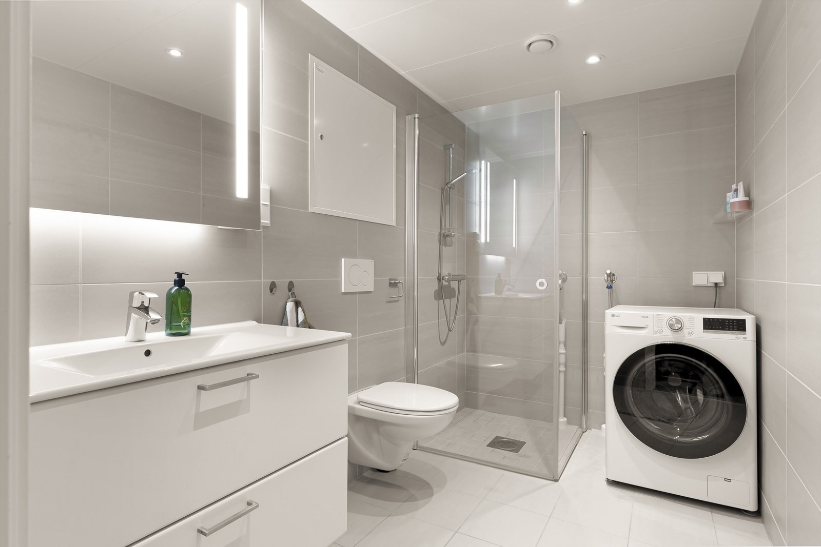 Moderne kabinbad fra 2020 med flislagte overflater, vegghengt toalett og opplegg for vaskemaskin. Galleribilde