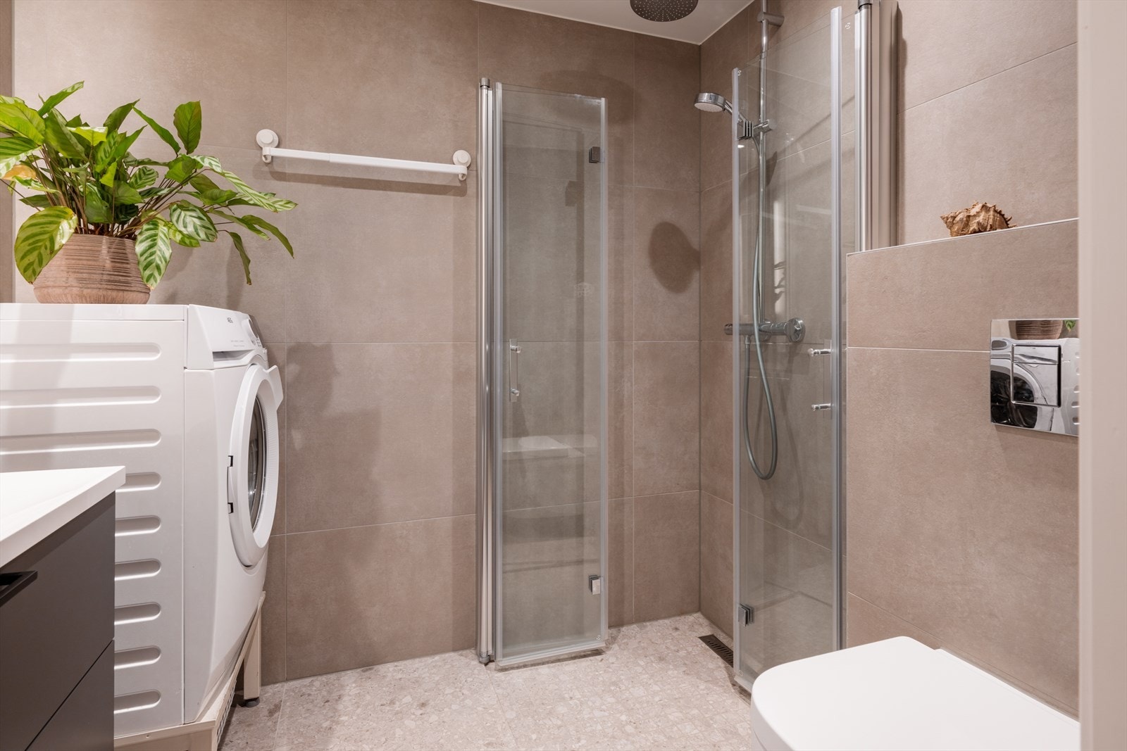 Romslig og pent bad i hybeldelen innredet med dusjnisje og innfellbare dusjdører, servant med ett-greps blandebatteri og vegghengt toalett. Galleribilde