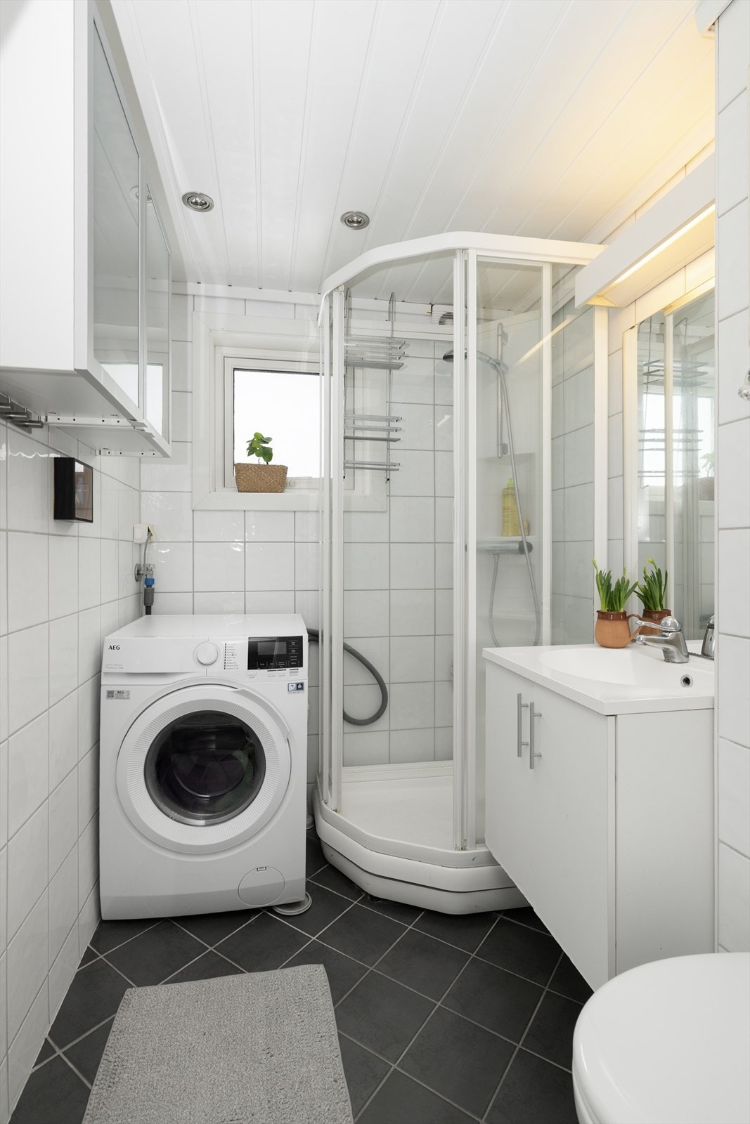 Pent bad fra 2006 med flis på gulv og vegger. Her er det dusjkabinett, vegghengt toalett og innredning med heldekkende vask, underskap med slette fronter, speil og lys. Ekstra oppbevaringsplass i overskap.
Opplegg for vaskemaskin, varmekabler og el-vifte. Galleribilde