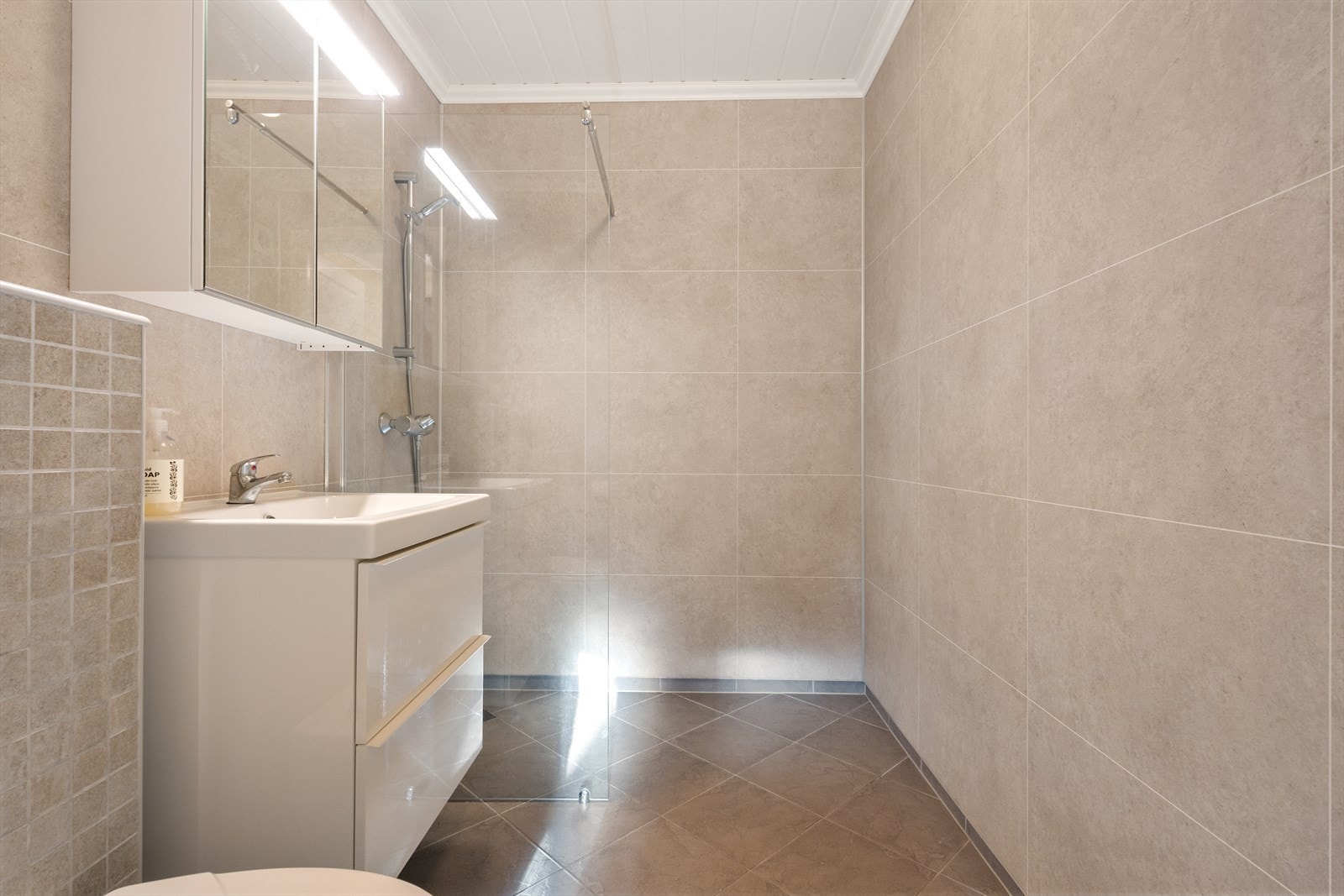 Innredet med servant i møbel, speilskap, vegghengt toalett og dusj med glassdør. Galleribilde