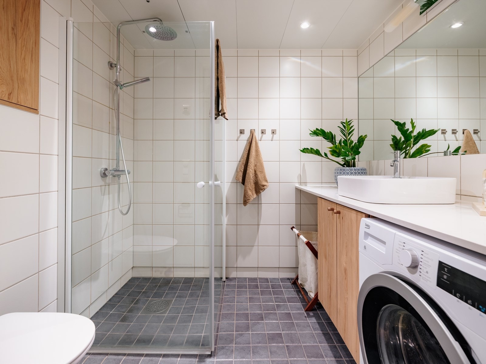 Lyst, flislagt bad med tidløse fliser samt innredning med trefronter. Varmekabler i baderomsgulv sørger for varme føtter året rundt. Galleribilde