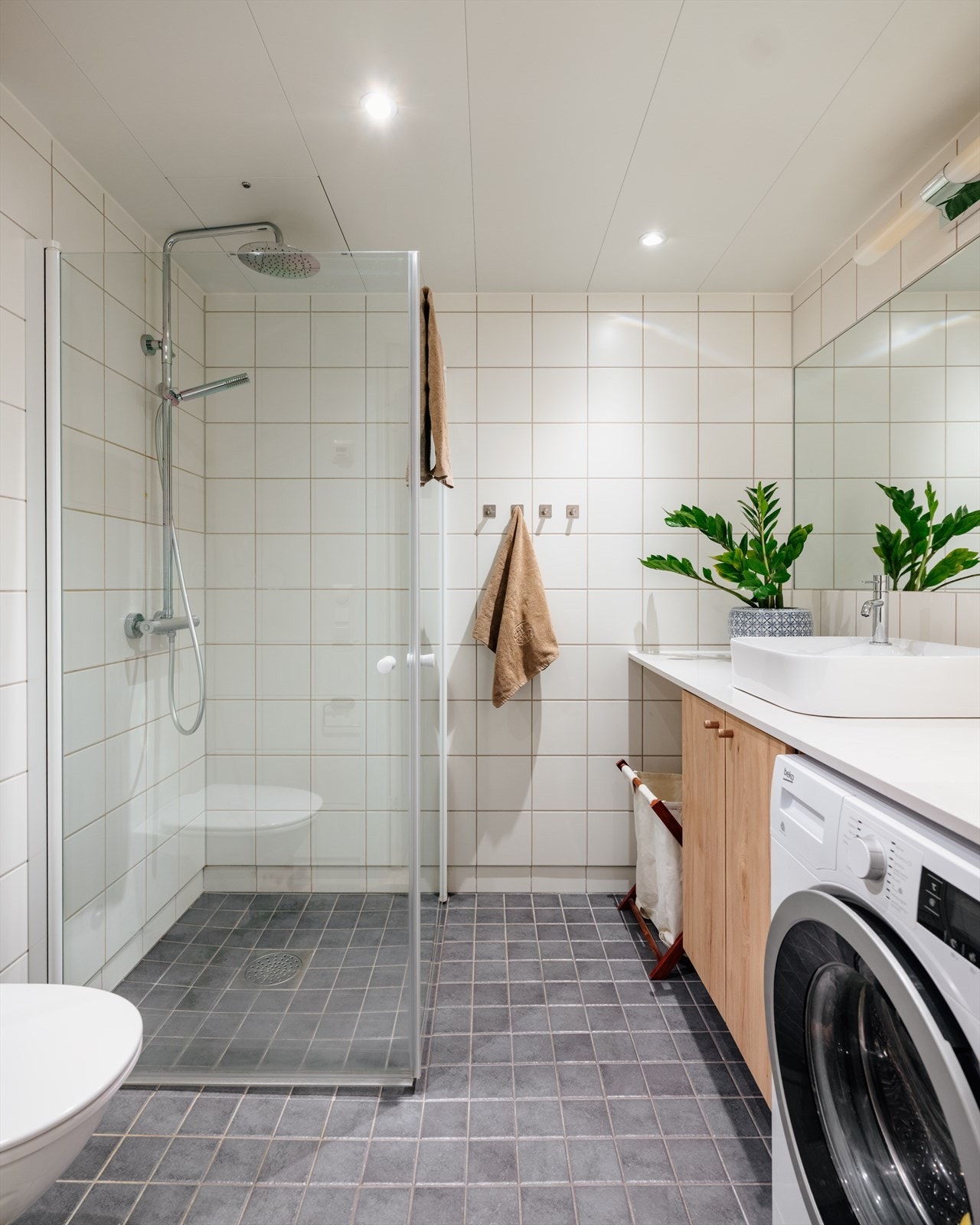 Badet er innredet med speil, servant på servantskap, vegghengt toalett, dusjhjørne og opplegg for vaskemaskin. Galleribilde