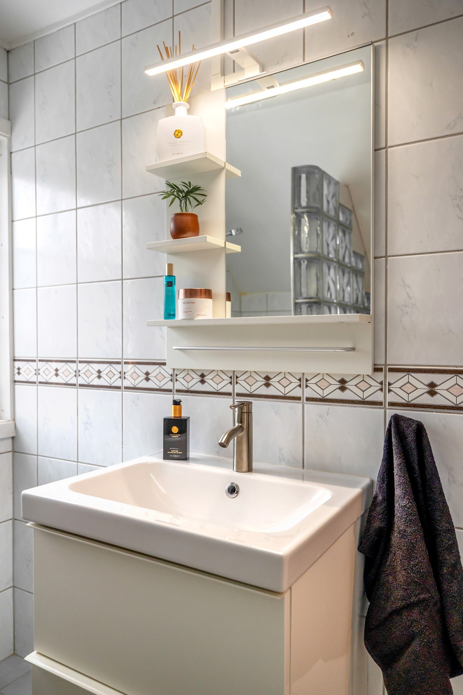 Badet er innredet med servant med underskuff, speil med belysning og hyller, toalett samt dusjsone avskjermet med glassbyggerstein. Galleribilde