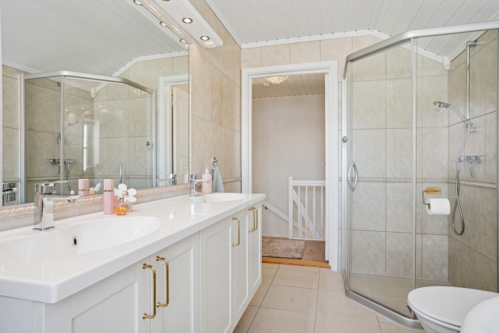 Badet har servant med dobbelt vask og oppbevaring under i skapene. Vegghengt speil med montert belysning over speilet. Toalett og dusjhjørne. Galleribilde