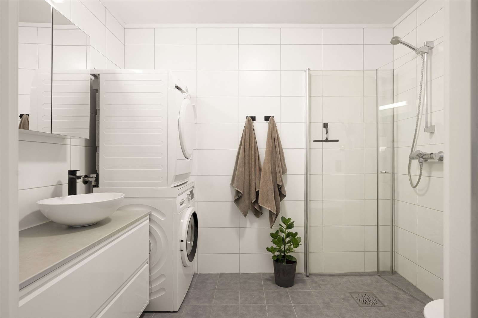 Badet har flislagte overflater, dusjhjørne med glassdører og opplegg for vaskesøyle. Galleribilde