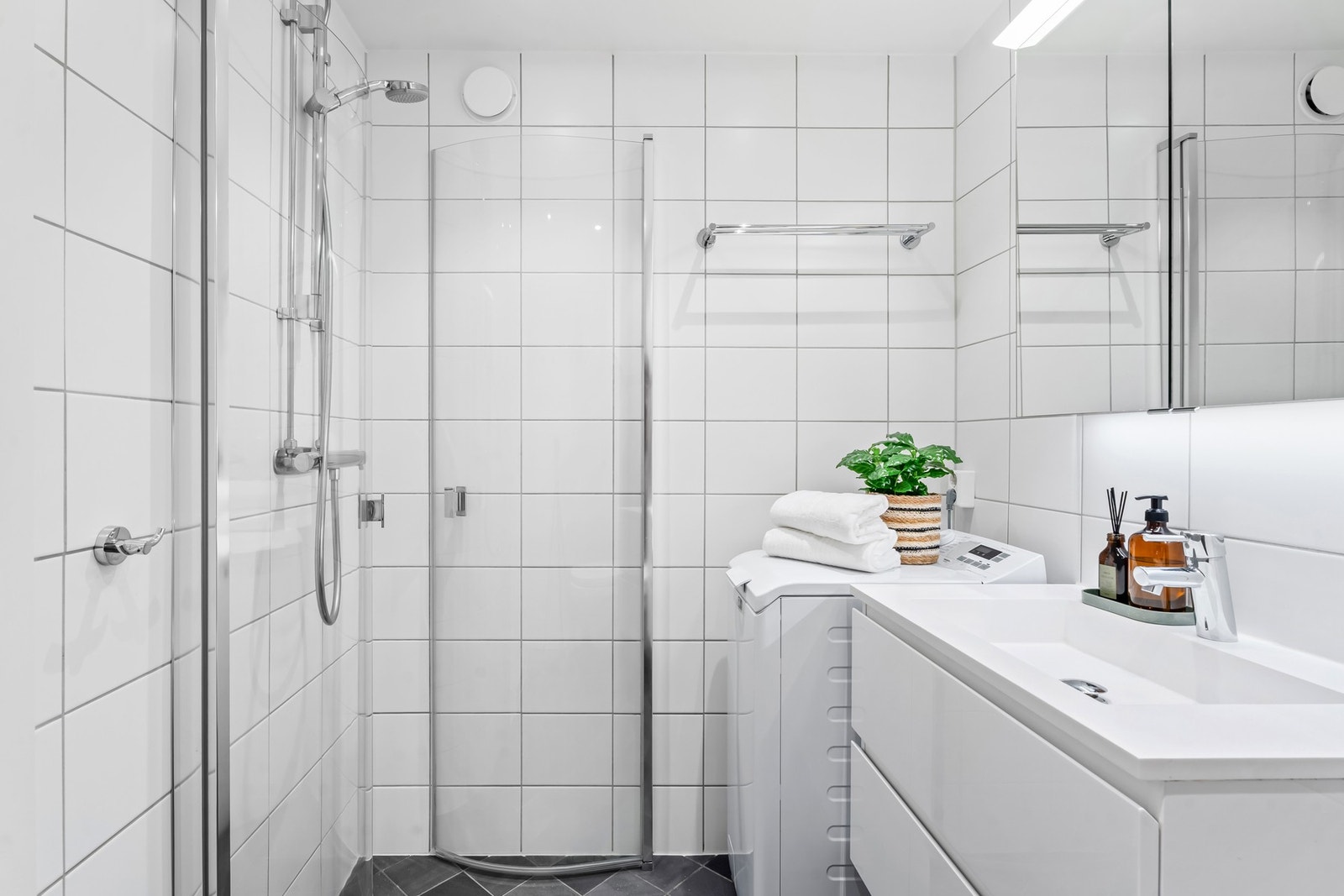 Badet har opplegg for vaskemaskin og et dusjhjørne med innfellbare dusjdører i glass. Galleribilde