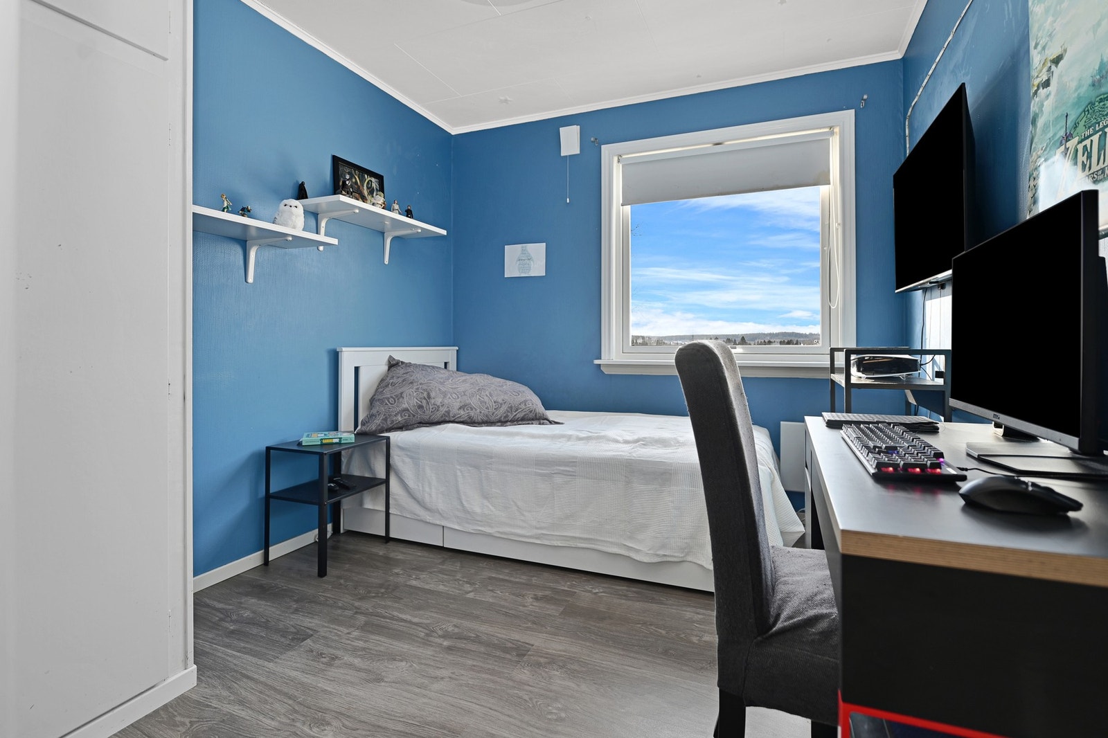 Soverom med blå vegger, stort vindu, laminatgulv og god plass til seng og skrivebord. Galleribilde