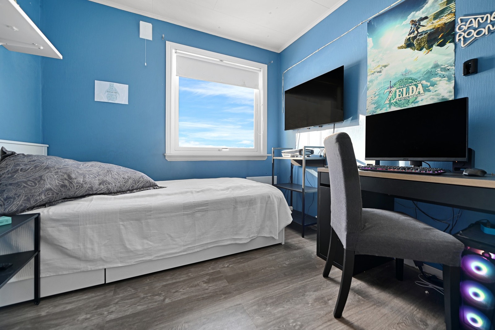 Rommet har blå vegger, stort vindu og skrivebord med skjerm. Galleribilde