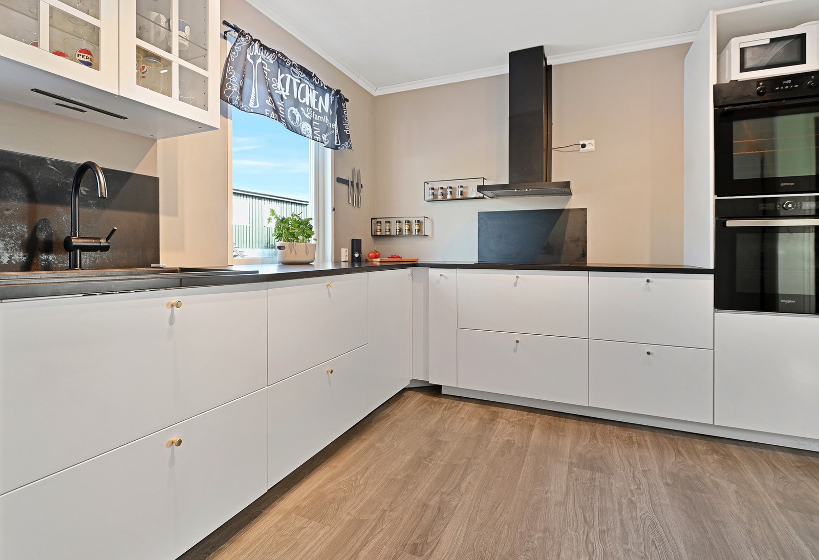 Moderne kjøkken med lyse flater, innebygd komfyr og ventilator. Store vinduer gir godt med naturlig lys. Galleribilde