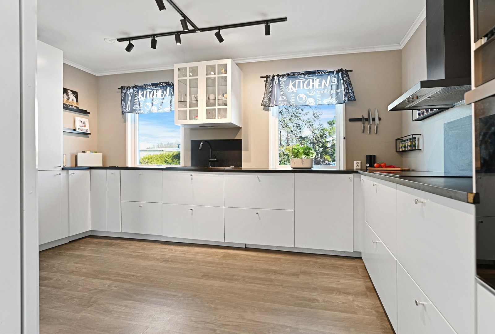 Moderne kjøkken med hvite skapfronter, integrerte hvitevarer og god benkeplass. Store vinduer gir naturlig lysinnslipp. Galleribilde