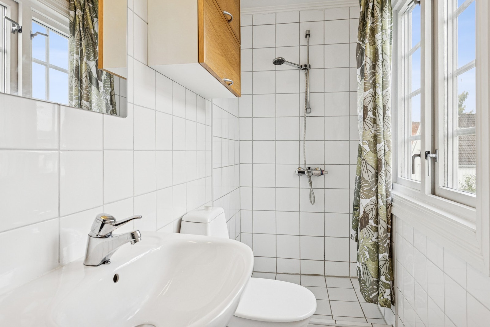 Et av boligens flere bad, hensiktsmessig utformet med dusj, servant og veggmontert oppbevaring. Dette fra boligens hybel. Galleribilde