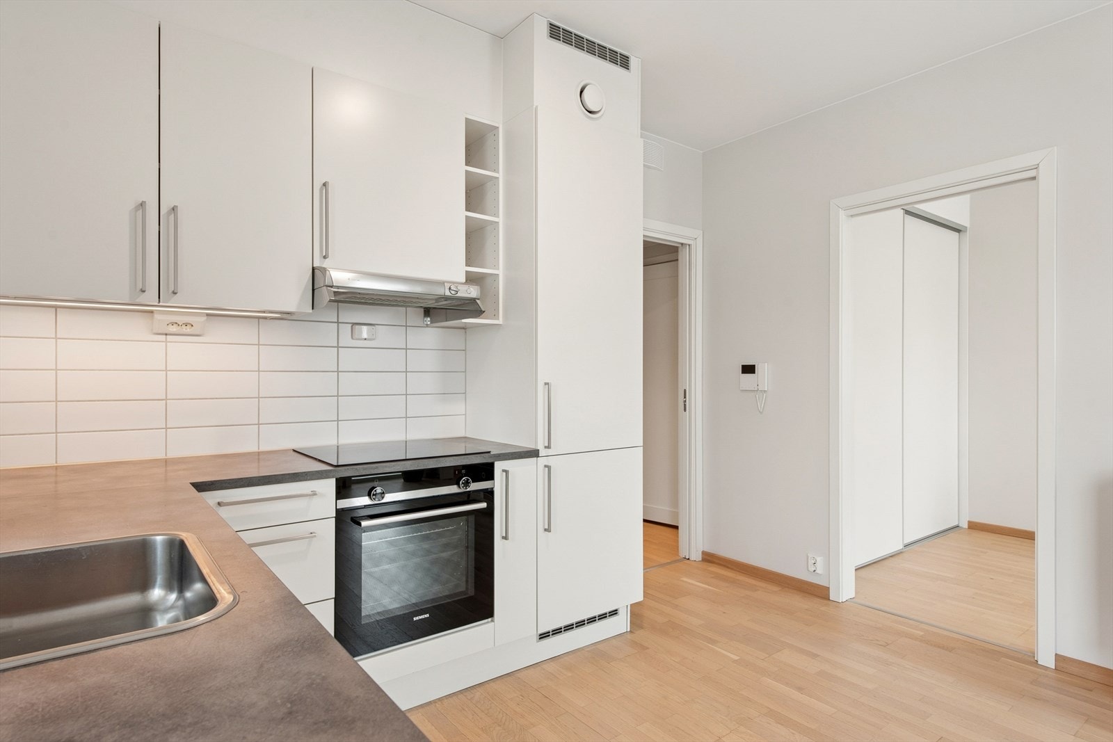 Kjøkkenet fra 2020 fremstår moderne og stilrent, med hvite, glatte fronter og en mørk laminatbenkeplate med nedfelt, rustfri oppvaskkum. Galleribilde