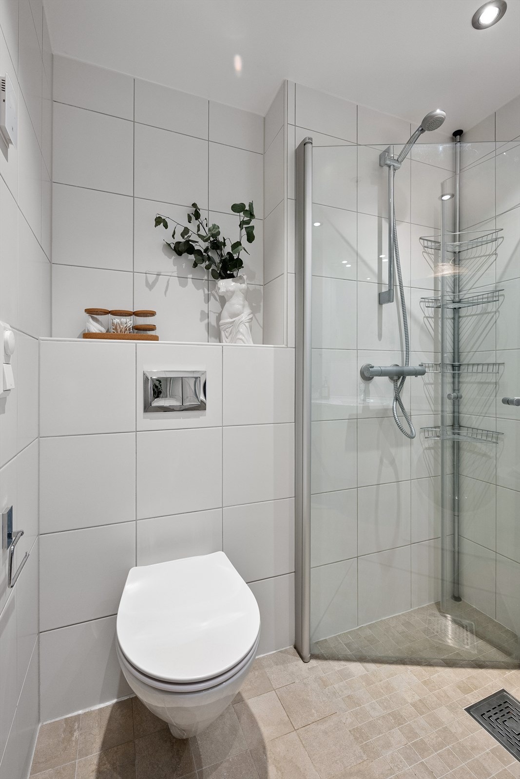 Dusj på gulv i hjørnet med innfellbare dører, dusjbatteri tilkoblet veggmontert hånddusj, vegghengt servantskap med skuffer, ovenpåliggende servant, vegghengt toalett, speil, overlys og stikkontakt på vegg over servant. Nedsenket himling med downlights Galleribilde